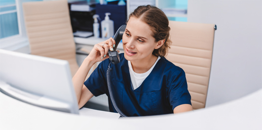 Photo of a woman talking on phone in clinic while sitting and looking at computer